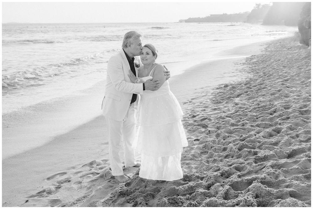 Couple embracing during a family beach photo session at Dreams Bahia Mita, with ocean waves behind them.