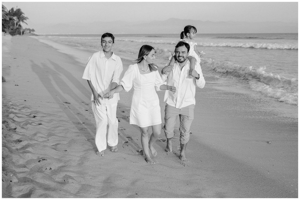 Family beach photos in Dreams Bahia Mita, with a child riding on dad’s shoulders as they walk together along the sandy shore.