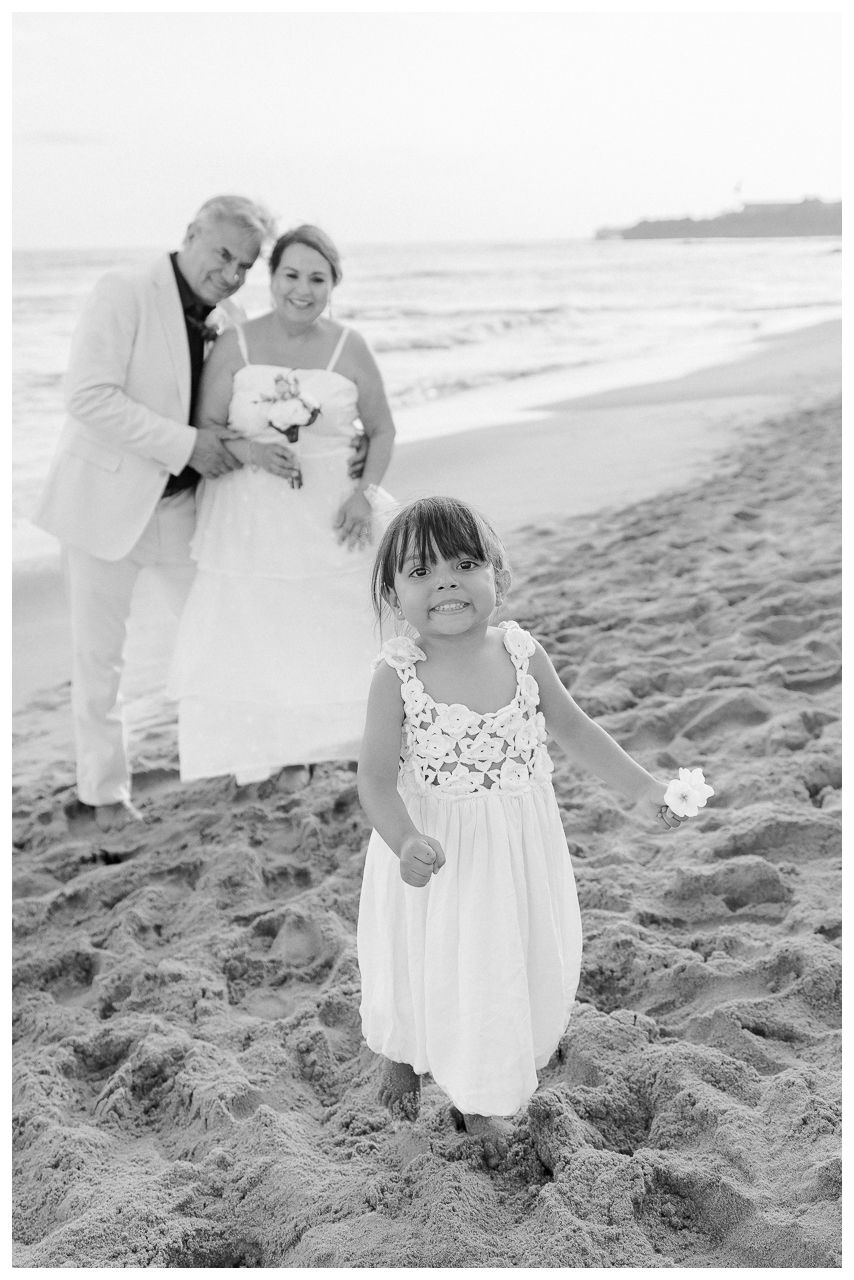 Grandparents sharing a beach photo session with their granddaughter at Dreams Bahia Mita, smiling together by the shore.
