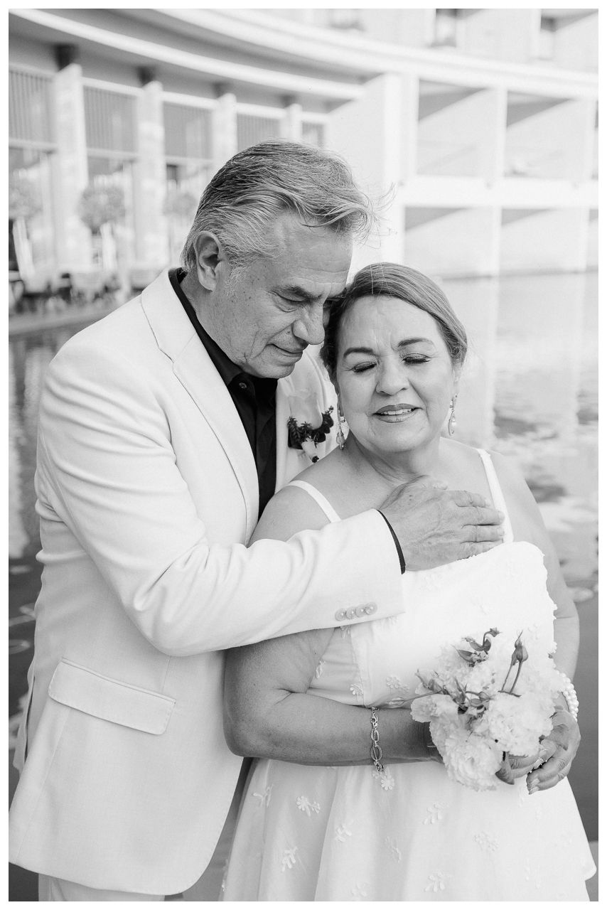 Couple embracing during an anniversary celebration in Dreams Bahia Mita, with a white bouquet by the waterfront.
