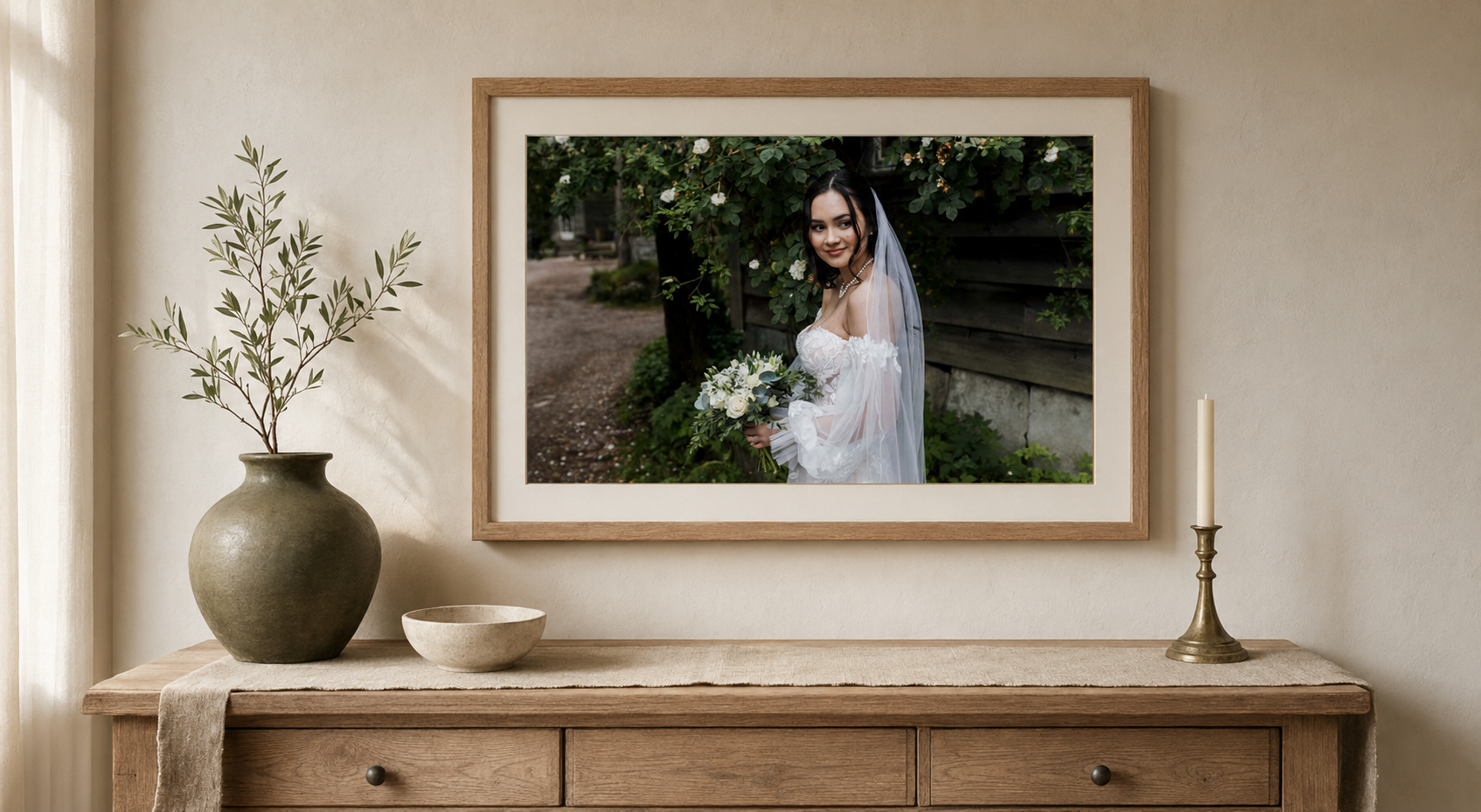 Framed wedding photo of a bride holding a bouquet, displayed above a wooden console table with a vase and candle.