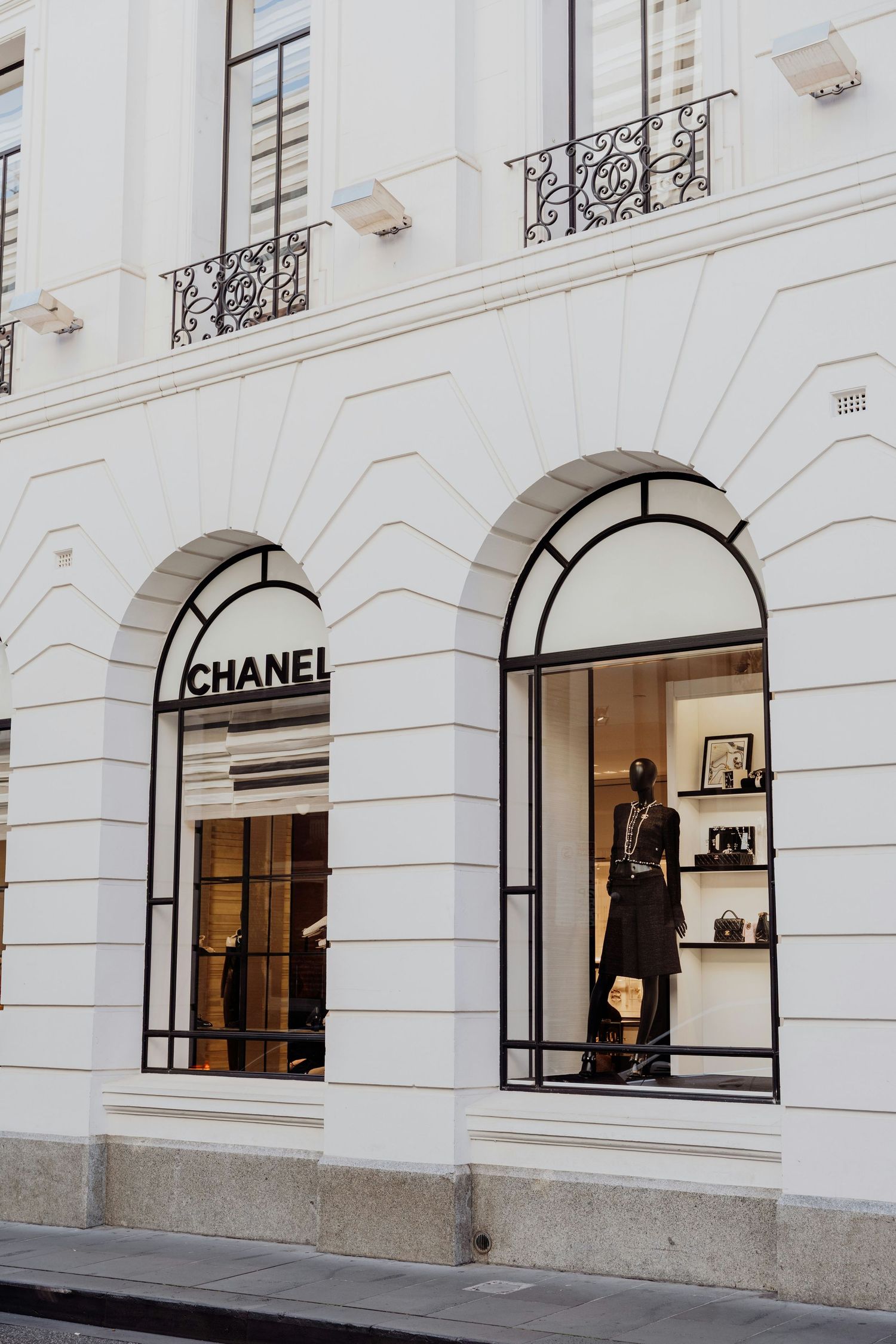 Elegant Chanel boutique storefront with arched windows, mannequin display, and classic white facade architecture.