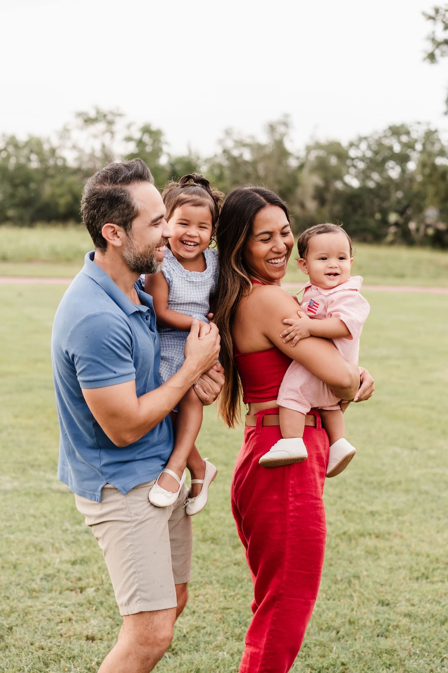 A family of three posing together outdoors in a park setting during golden hour.