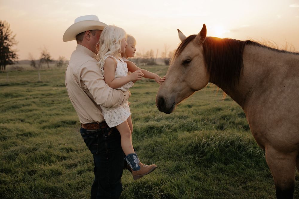 A cowboy holding his girl in a sunlit field as they gently pet thier horse for thier family photography photoshoot in red deer alberta farm