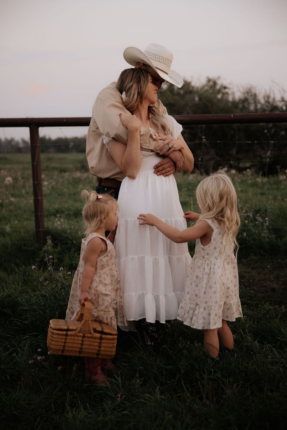 Family in rustic outfits with two young girls in a green field at dusk.