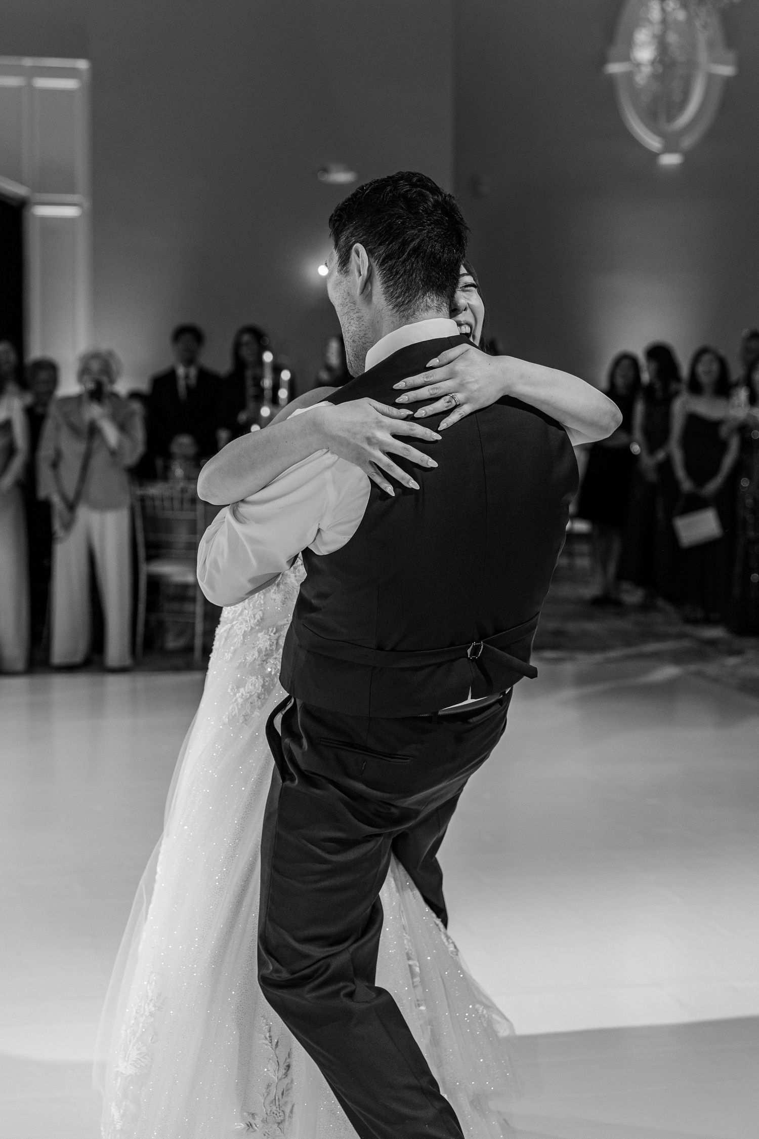 Black and white photo of a bride and groom sharing their first dance at an elegant wedding reception.