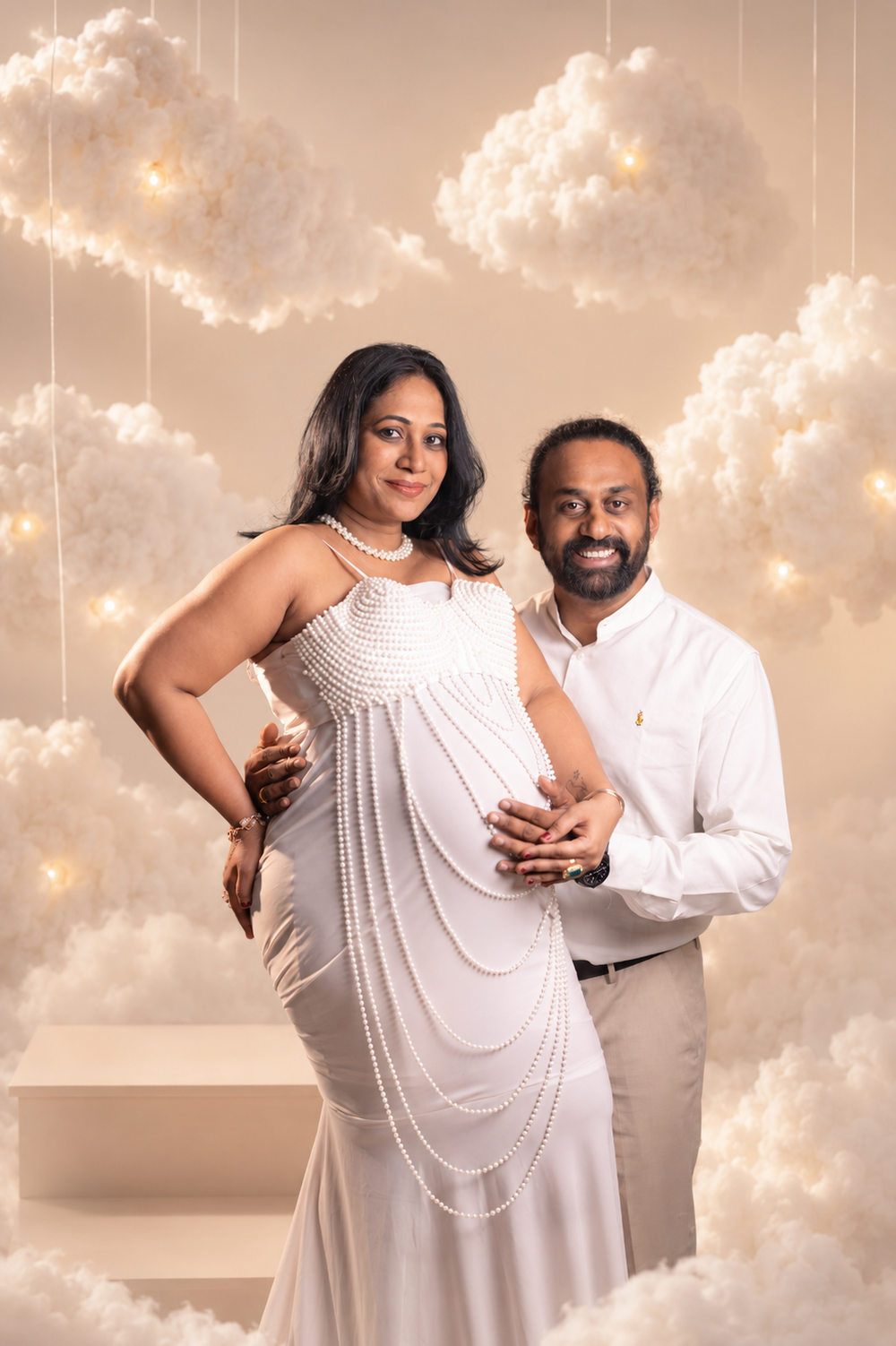 Pregnant couple in white outfits posing together in a dreamy cloud-themed maternity photo shoot.