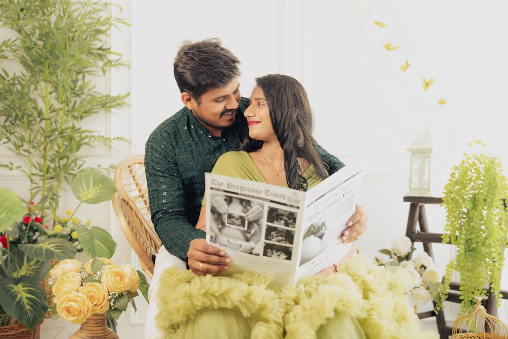 Couple in traditional Indian attire sharing a romantic moment while holding a photo album surrounded by lush greenery.