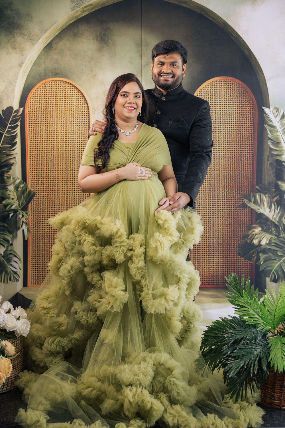 Pregnant woman in olive green tulle gown poses with partner in black suit for maternity photoshoot.