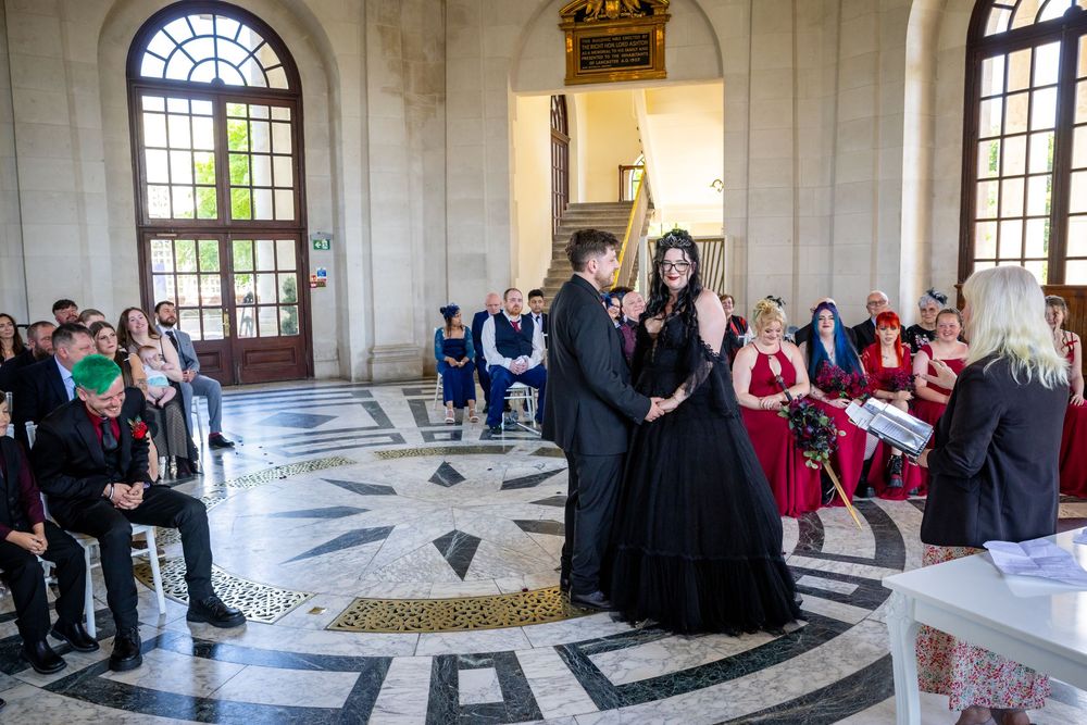 Gothic wedding ceremony in ornate hall with couple in black attire exchanging vows before seated guests.