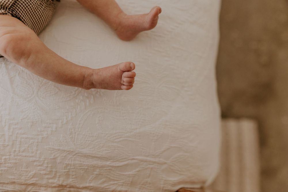 Close-up of tiny newborn baby feet resting on a soft white textured blanket.