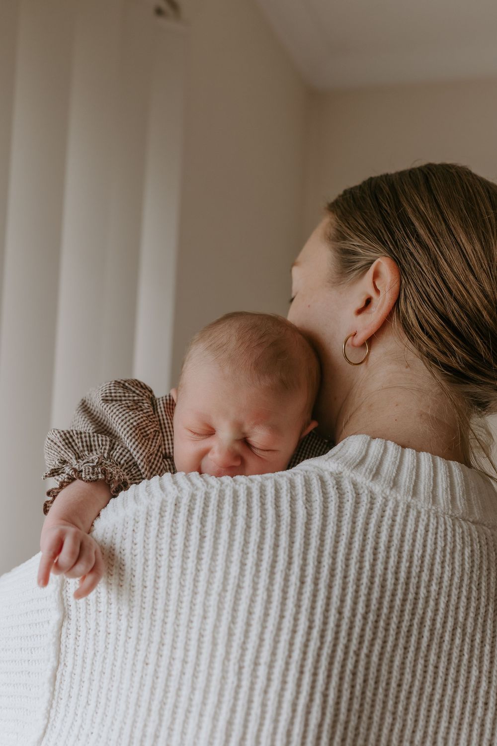 A mother gently holding her sleeping newborn baby against her shoulder in a soft natural light setting.