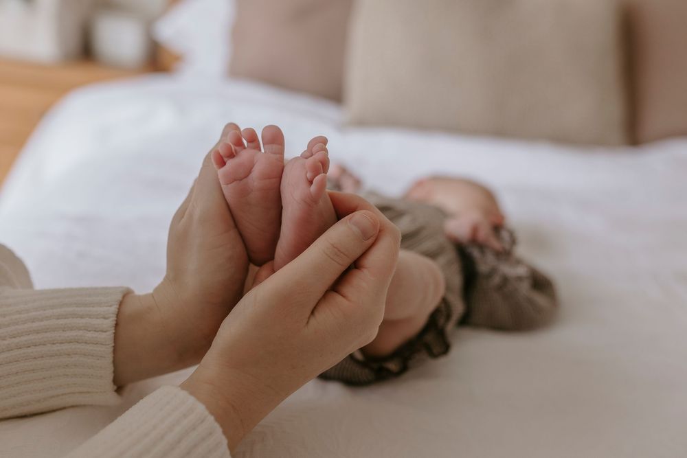 Adult hands gently cradling tiny newborn baby feet on a white bed.