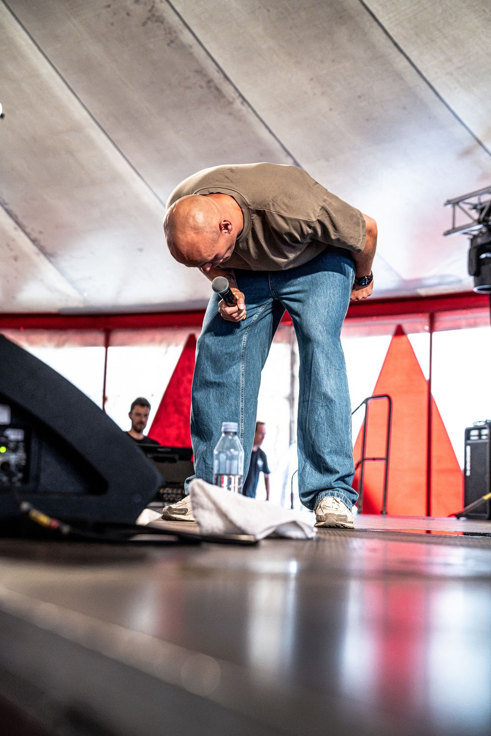 Performer bending forward on stage holding a microphone during an outdoor concert event.