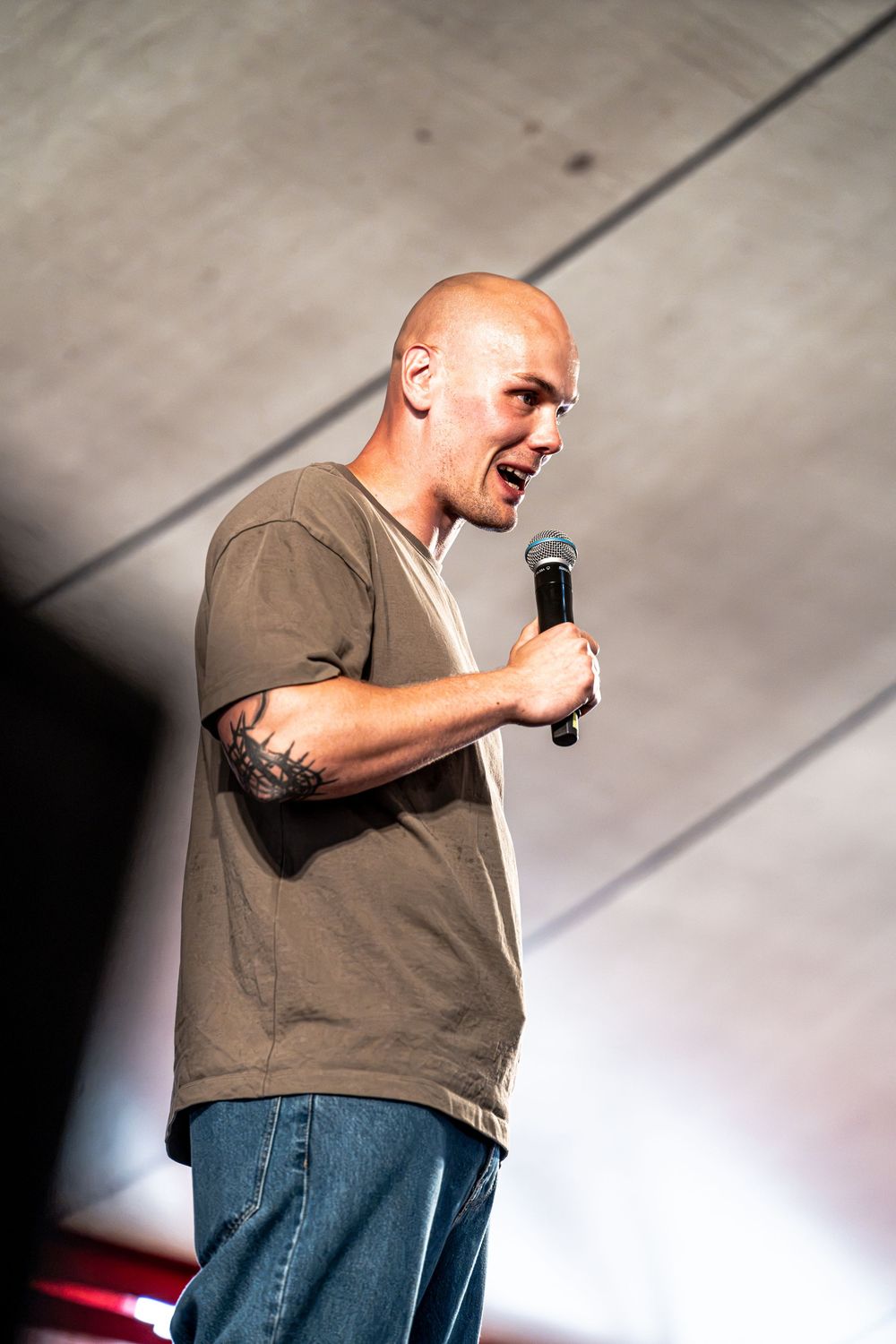 Bald tattooed performer passionately speaking into a microphone on an outdoor concert stage.