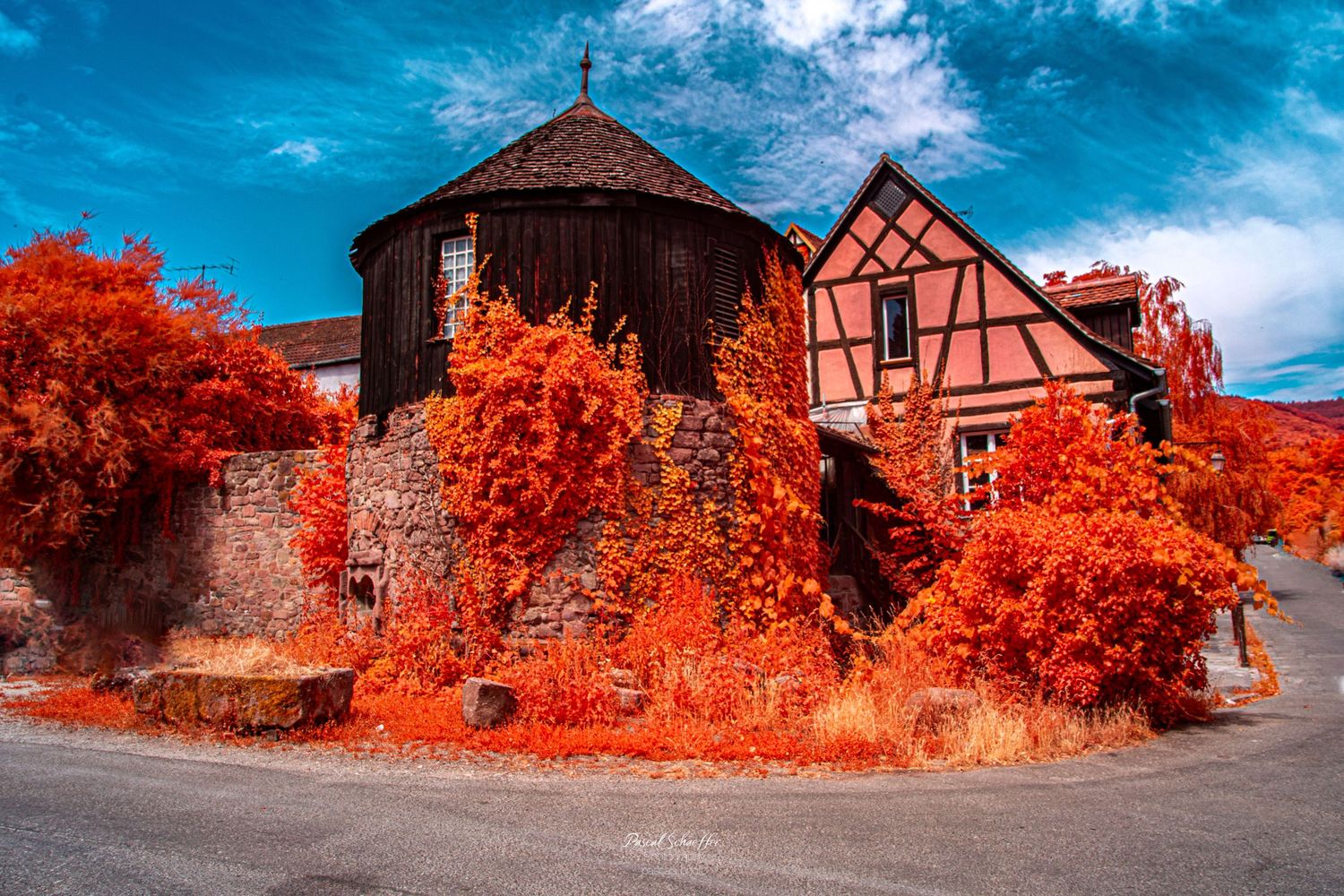 Infrared photo of a historic half-timbered house with vibrant red foliage climbing stone walls under a vivid blue sky.