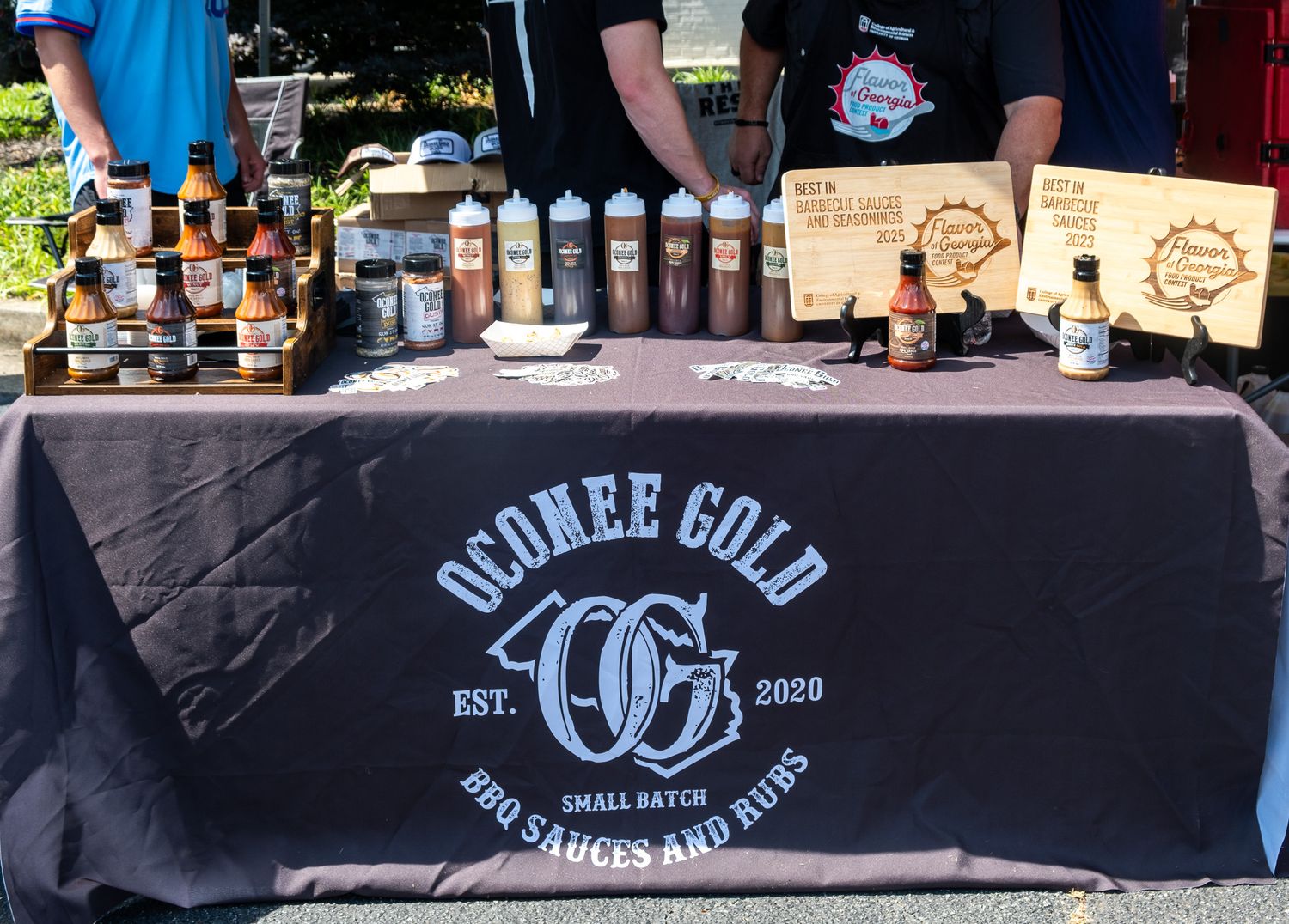 Oconee Gold Small Batch BBQ Sauces and Rubs display table with bottles and products at a Nichole Meshad Photography event photo shoot.