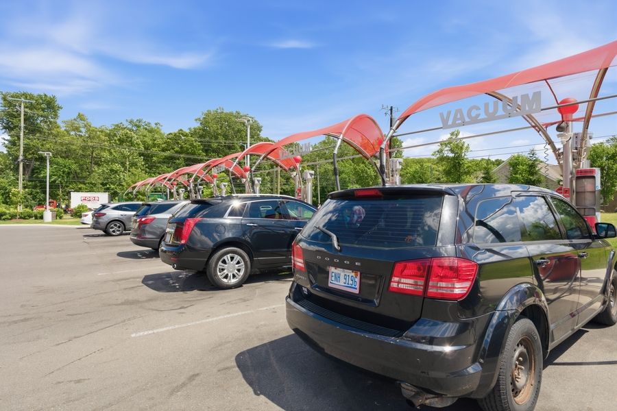 Cars lined up at a red car wash vacuum station under a bright blue sky.