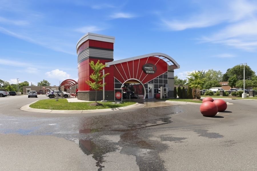 Red and silver modern fast food restaurant exterior with decorative apple sculptures in a sunny parking lot.