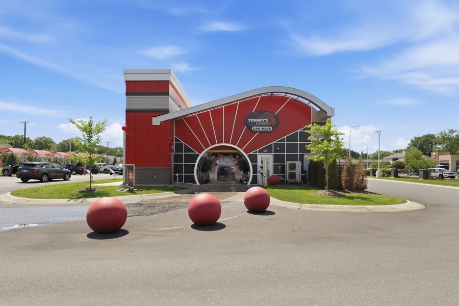 Vibrant red commercial building with decorative spheres in parking lot under blue sky, featuring bold sunburst architectural design.