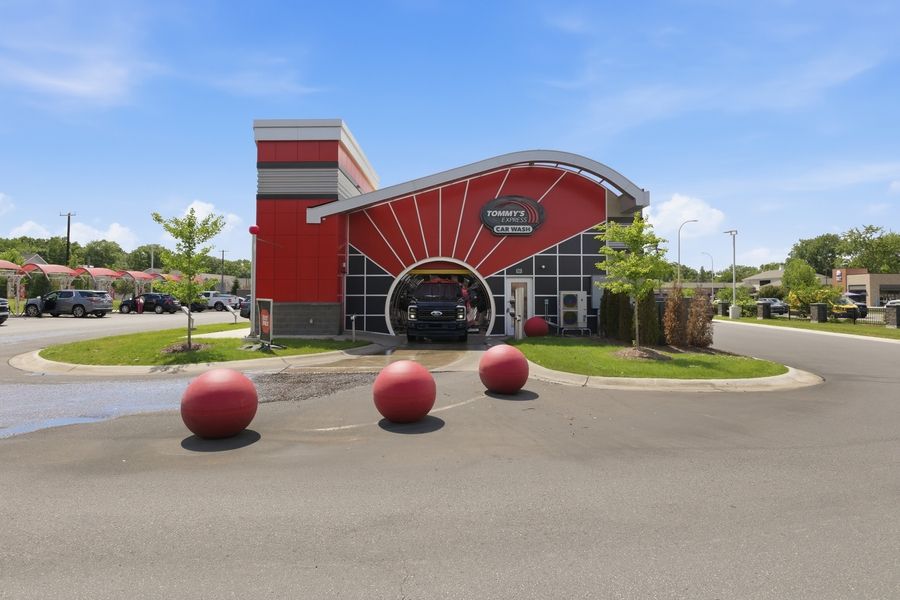 Red and black car wash building with decorative red spheres in foreground under blue sky.
