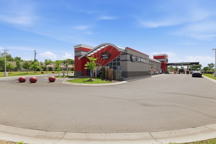 Modern car wash facility with red and black exterior design, featuring a spacious parking lot under a clear blue sky.