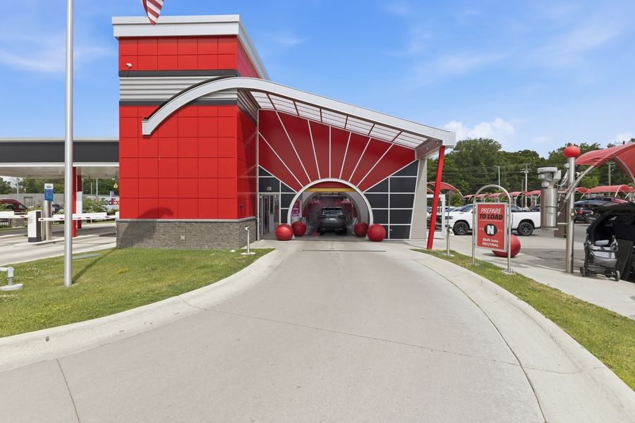 Red Tommy's Express car wash tunnel entrance with curved canopy architecture on a sunny day.