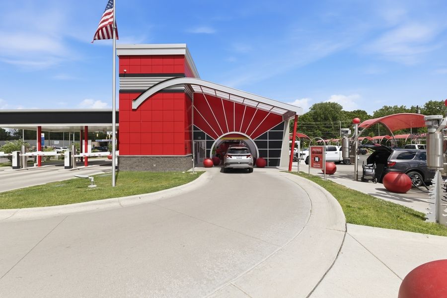 A car entering a red and silver car wash facility with covered lanes and an American flag.