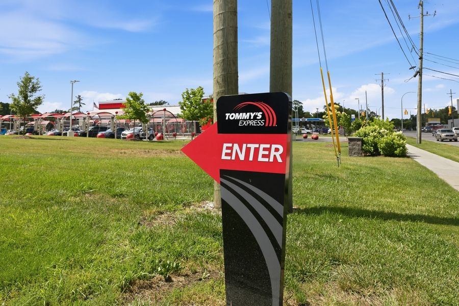 Tommy's Express car wash red arrow entrance sign mounted on post directing customers to enter.