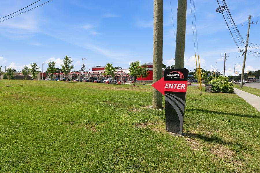 Car wash facility entrance sign with red arrow on a sunny day, surrounded by green grass and trees.