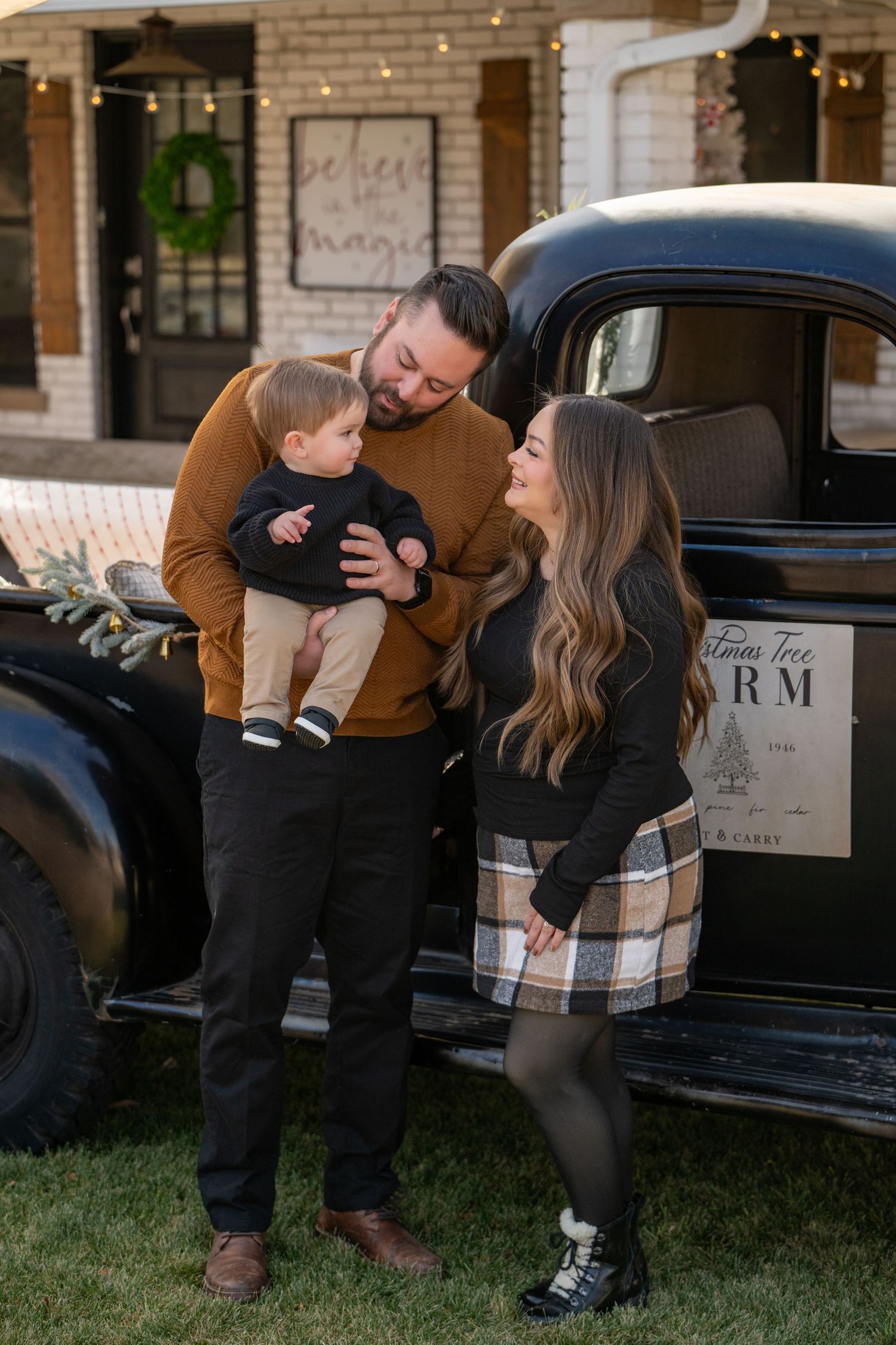 Family of three posing by a vintage black truck outdoors during a festive Christmas mini session.