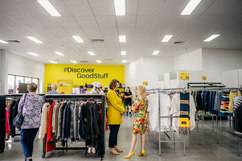 Shoppers browsing clothing racks inside a bright Good Sammy op shop with yellow branding.