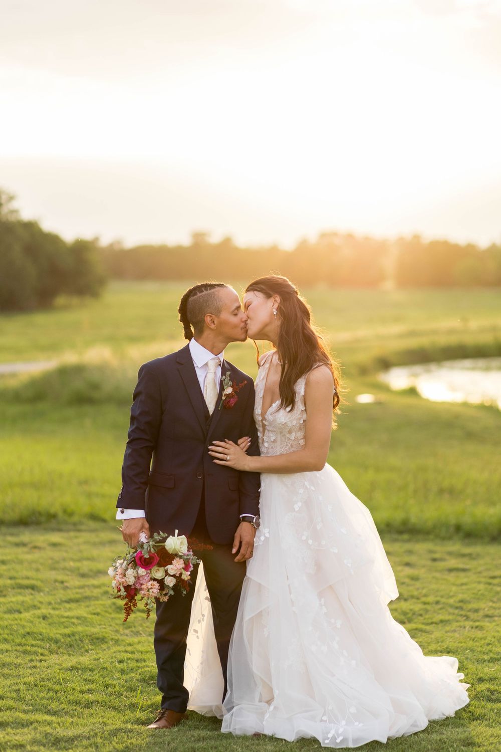 Bride and groom share a romantic kiss at golden hour on a lush green golf course, bride holding a colorful bouquet.