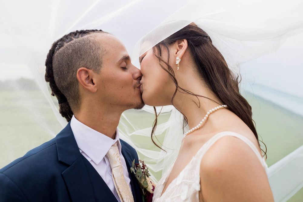 Bride and groom sharing a romantic kiss under a flowing white veil on their wedding day.