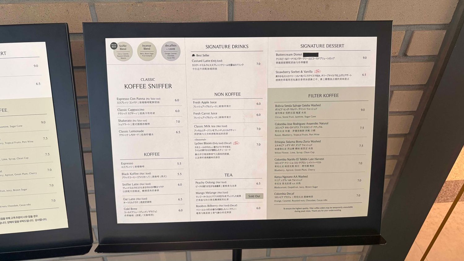A framed coffee shop menu board displaying signature drinks, hot coffee, and cold coffee options with elegant typography.