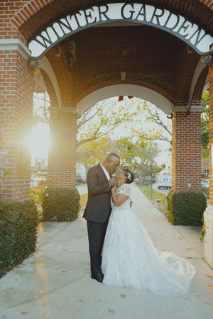 Couple shares romantic moment under Winter Garden arch in golden sunlight, bride in flowing white gown.