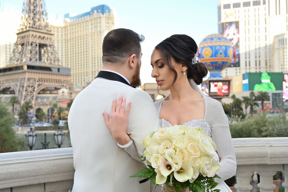 Newlywed couple posing on the Las Vegas Strip with the Eiffel Tower replica, bride holding white bouquet.