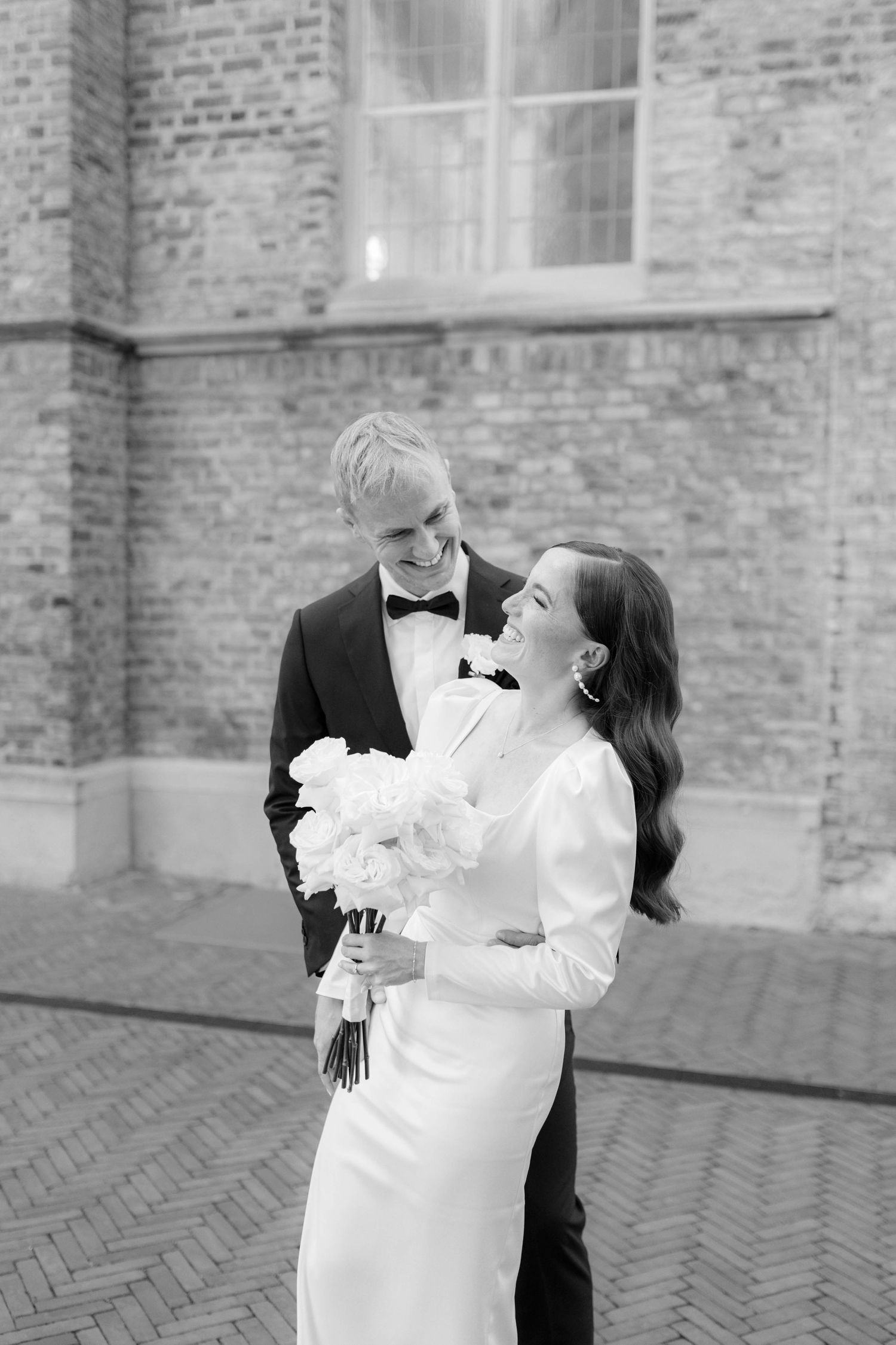 Black and white photo of a bride and groom sharing a romantic kiss outside a classic building on their wedding day.