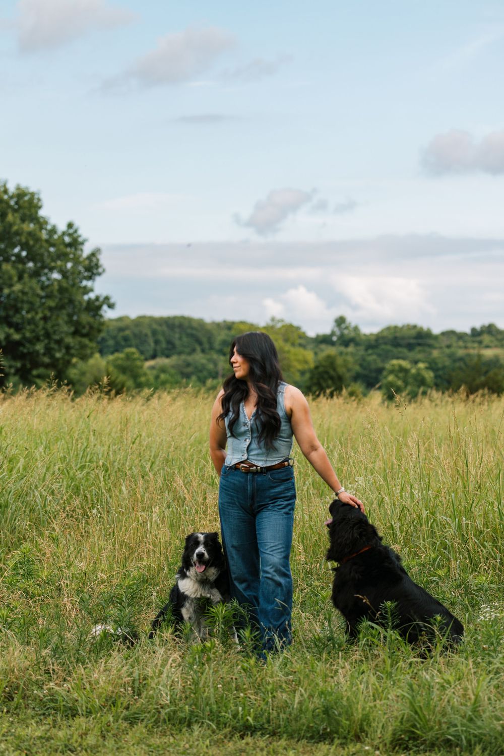 A girl poses with her two dogs in a pasture.
