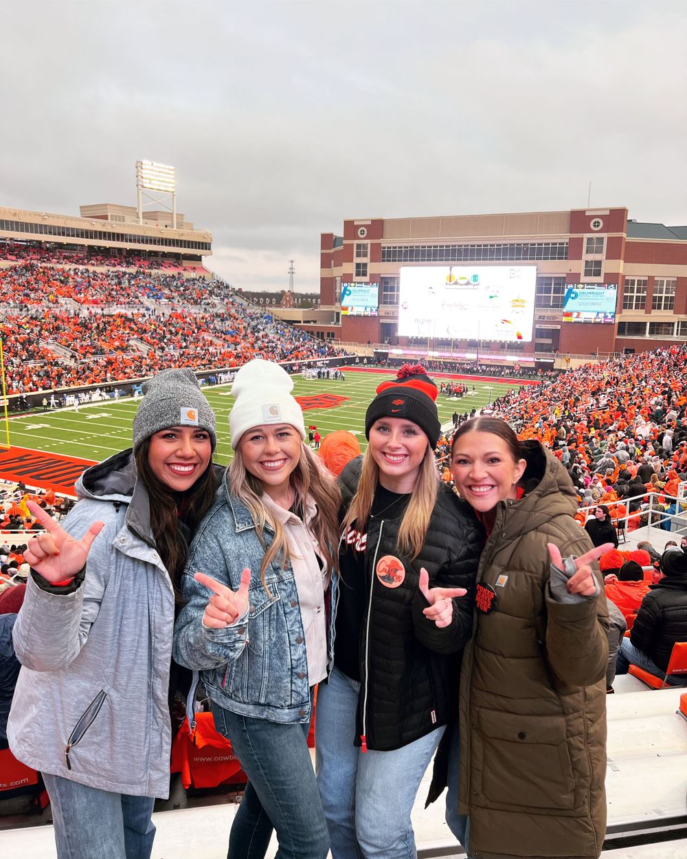 A group of girls pose in front of the Boone Pickens stadium at an Oklahoma State University football game.