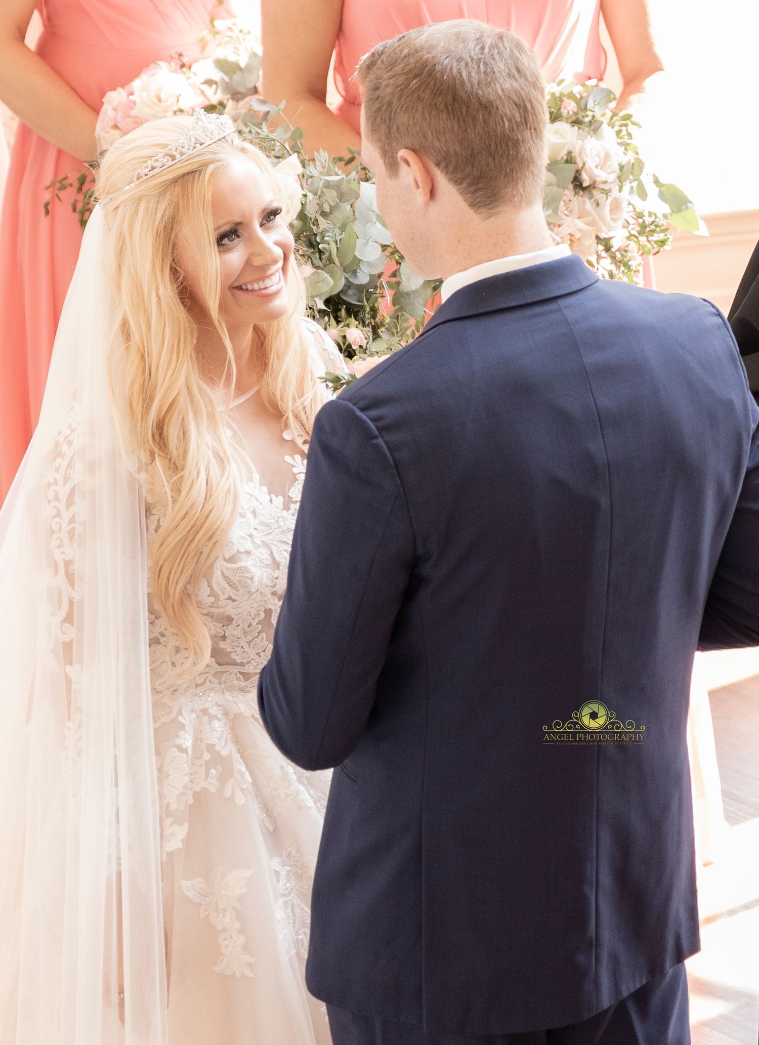 Bride and groom share first kiss at wedding ceremony while officiant raises hand in blessing.