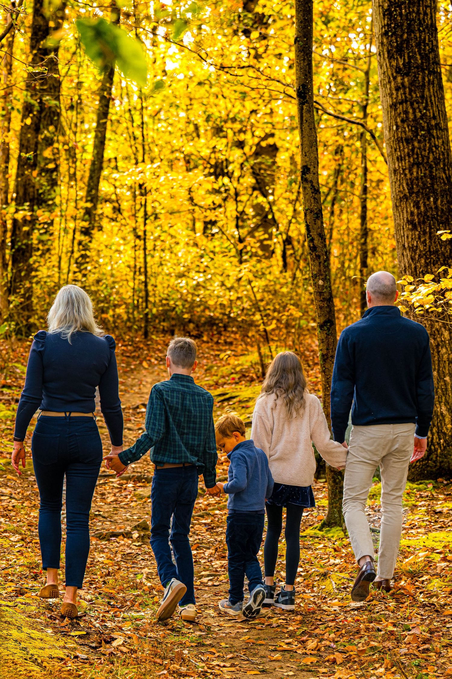Three children sitting on autumn leaves in a park surrounded by colorful fall foliage trees.