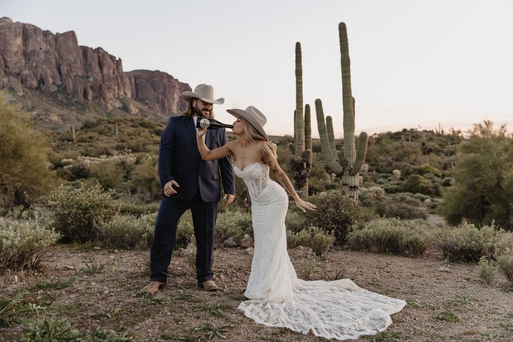 Couple in cowboy hats dancing in Arizona desert with saguaro cactus and Superstition Mountains backdrop.