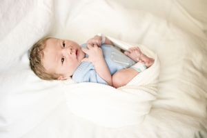 Newborn baby in light blue onesie lying on white fluffy blanket, looking up with bright eyes.