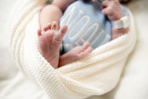 Close-up of newborn baby feet peeking out of a white swaddle blanket in a hospital setting.