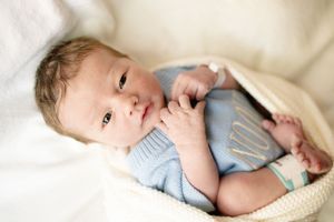 Newborn baby in a light blue knit onesie resting in a cozy basket with soft white blankets.