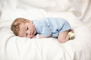 Newborn baby sleeping peacefully in a blue knit outfit on white bedding.