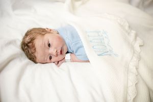 Newborn baby lying on a white knit blanket wearing a light blue outfit with an embroidered design.
