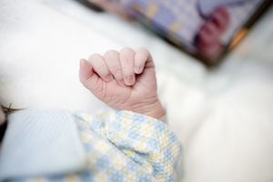 Close-up of a newborn baby's tiny clenched fist resting on a soft white blanket in a blue patterned onesie.