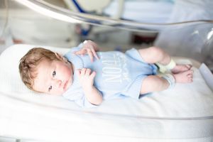 Newborn baby in blue onesie resting in a hospital incubator in the NICU under medical care.